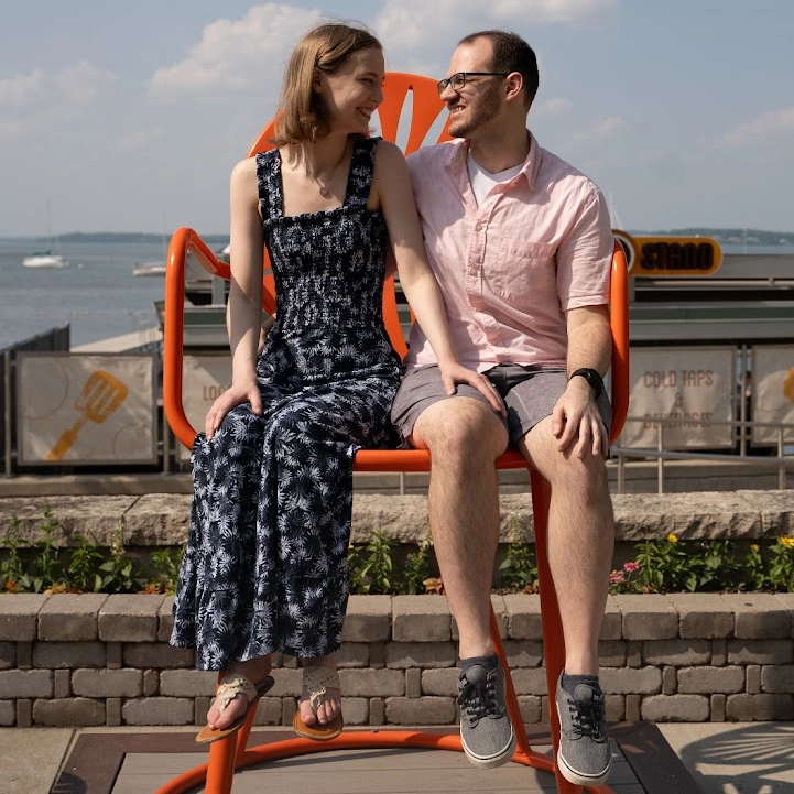 Samantha and Michael looking lovingly into eachothers eyes while sitting on a large chair in front of lake Mendota at the Memorial Union Terrace